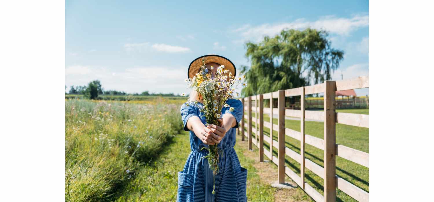 A woman in rustic dress with wildflowers on front of straw bales.