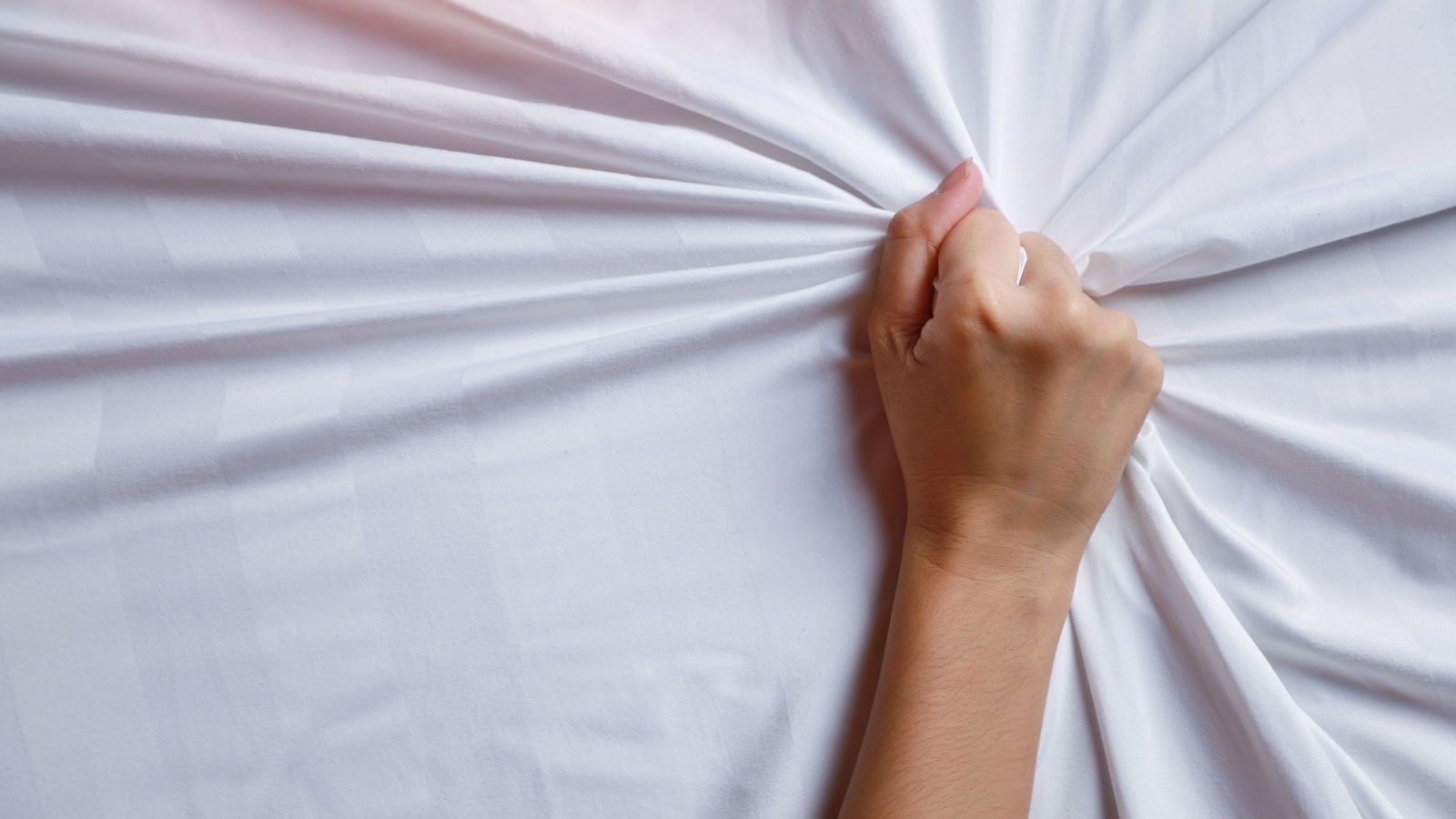 Close up young woman hands pulling white sheets in ecstasy