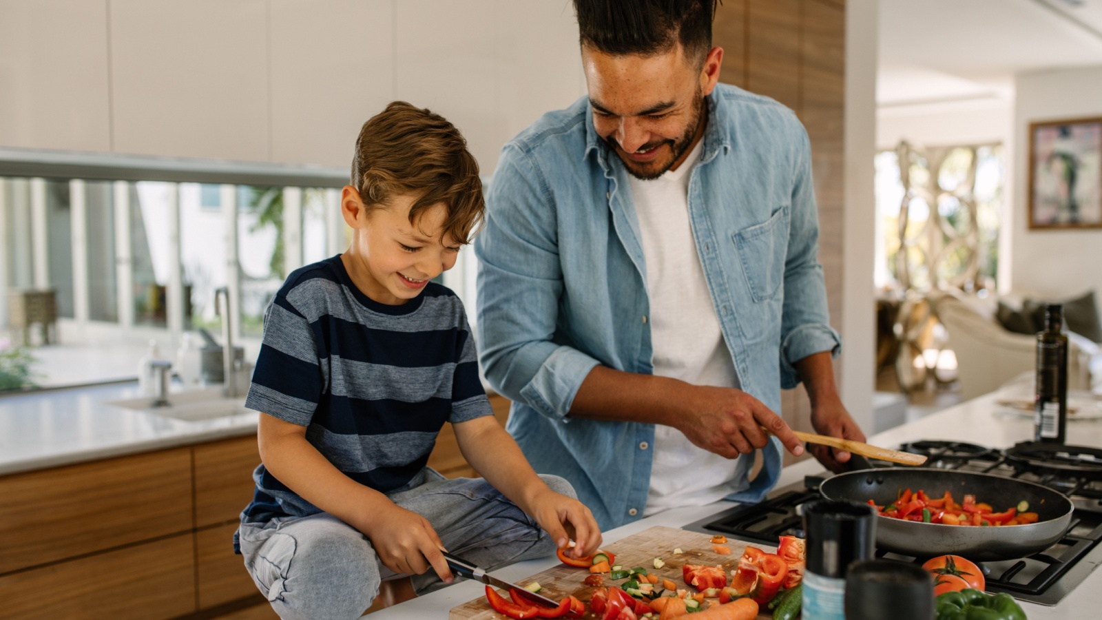 Little boy cutting vegetables with his father cooking food in kitchen