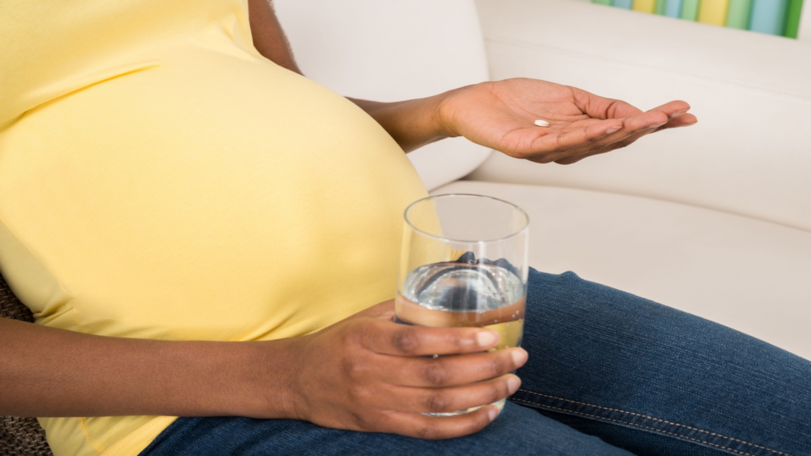 Close-up Of Pregnant Woman Holding Medicine With Glass Of Water At Home