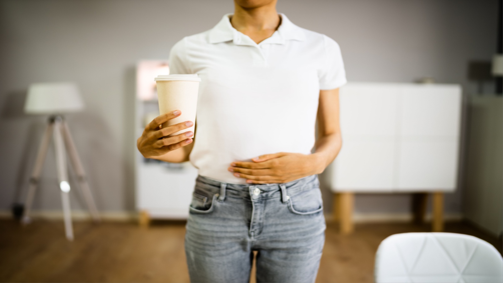 Person holding a cup of coffee with one hand and their stomach with another hand
