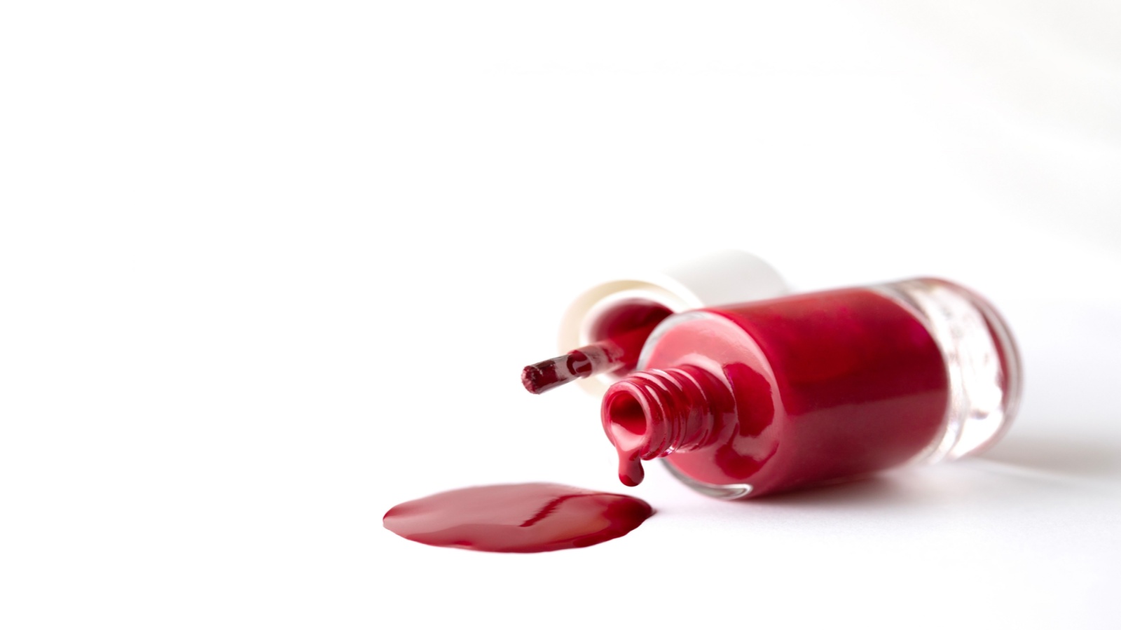 Red color polish nail pouring from bottle to white background
