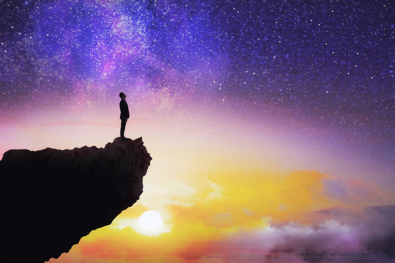 Man standing on edge of cliff with colorful sky