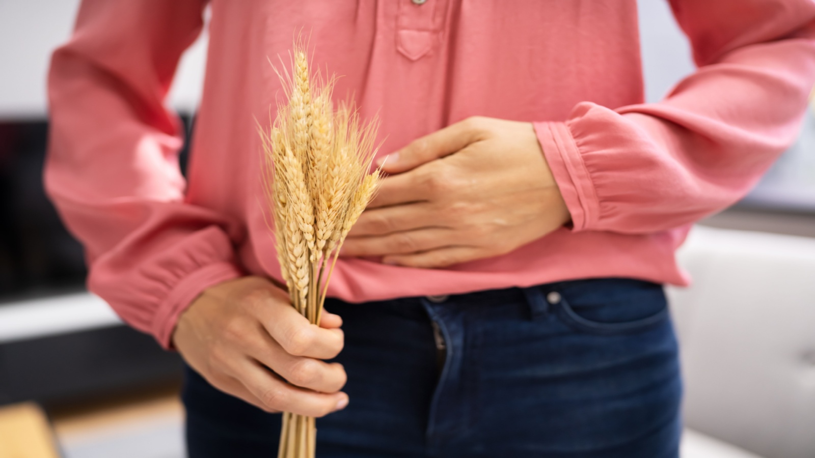 person holding a piece of wheat as well as holding stomach in pain; showing celiac disease