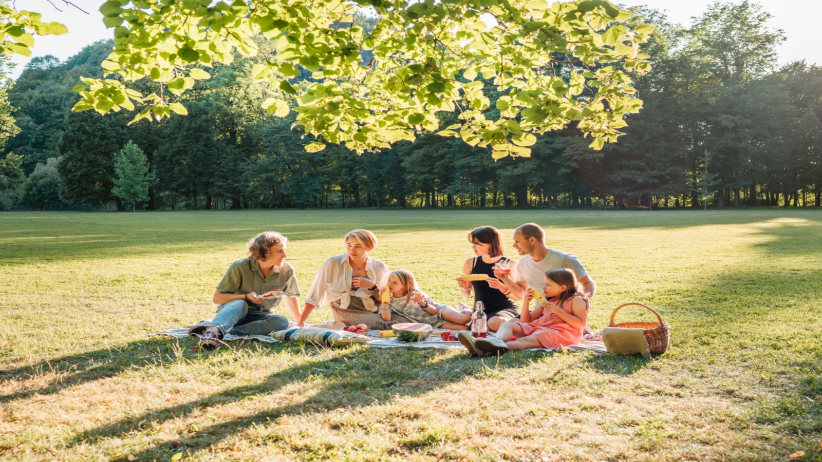 Big family sitting on the picnic blanket in city park during weekend Sunday sunny day