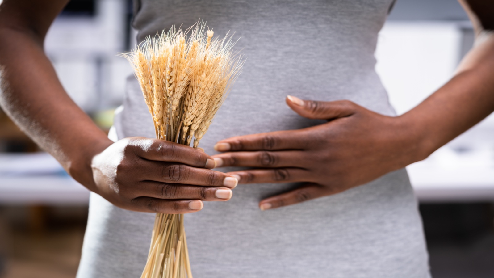 Black woman holding a handful of wheat and her belly, signifying celiac disease and gluten intolerance