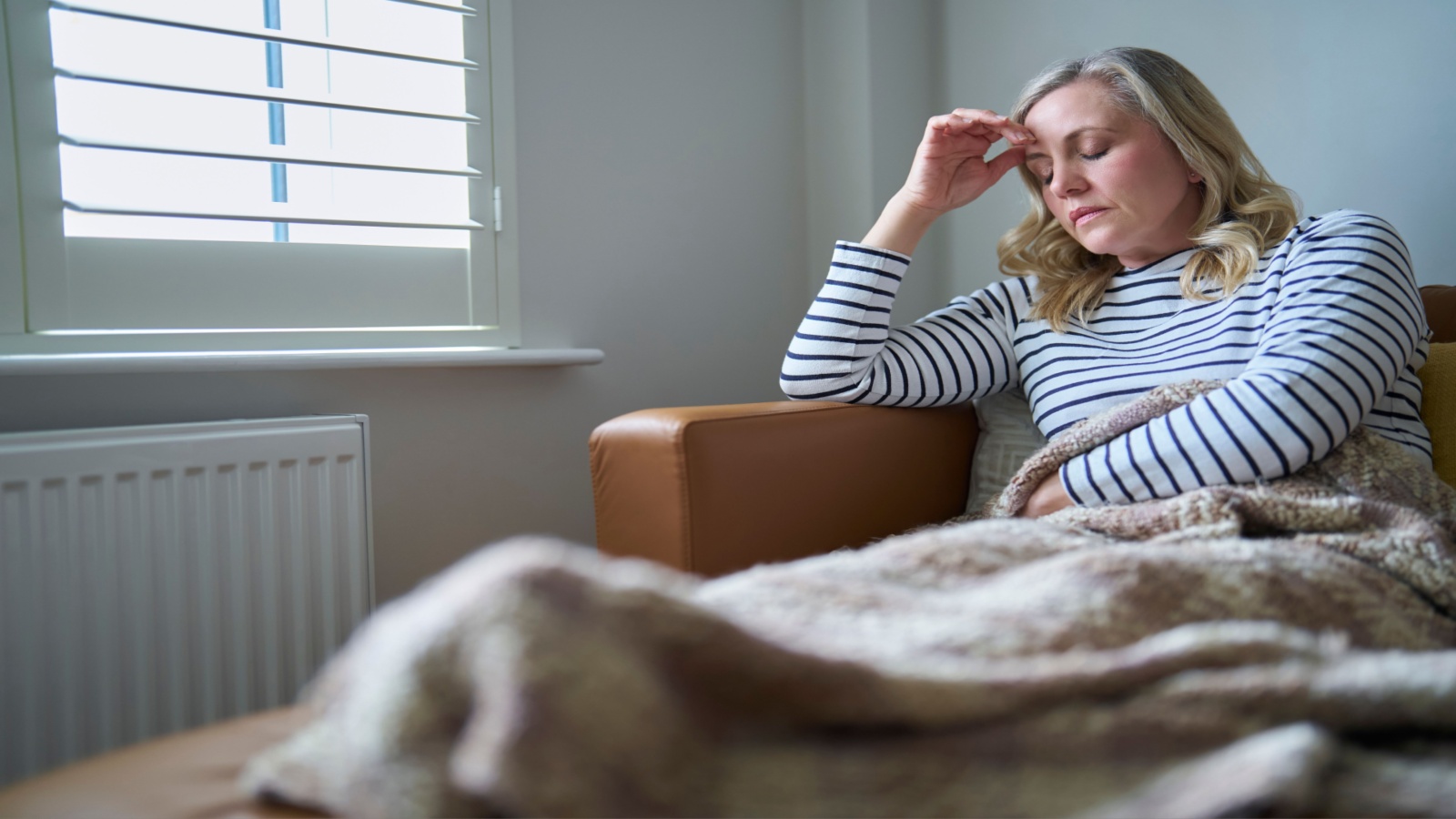 woman sitting on the couch rubbing her head in pain/fatigue, suffering from long COVID