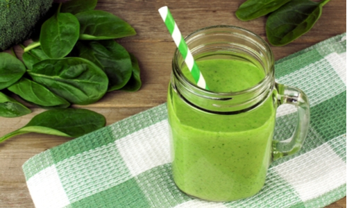 Healthy green smoothie with spinach in a jar mug with checkered cloth against wood