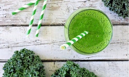Green kale smoothie overhead view, in a glass with straw on an aged wood background