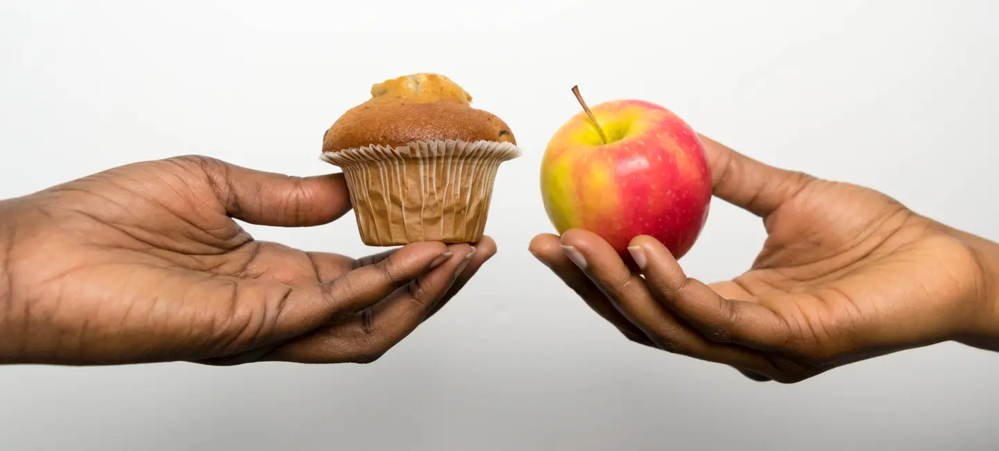 hands holding a cup cake and an apple