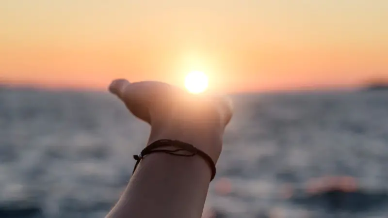 Female hand reaches for the sun at sunset against the background of the sea.