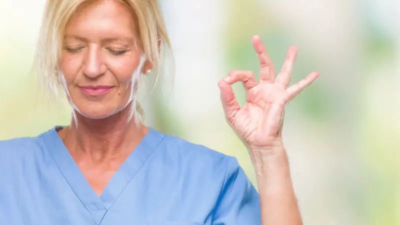 Nurse smiling with eyes closed doing meditation gesture with fingers Nurse smiling with eyes closed doing meditation gesture with fingers