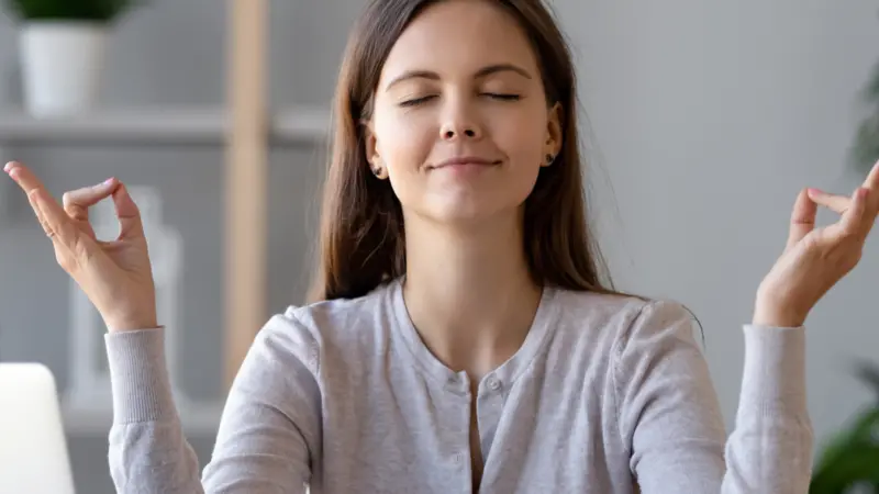 Calm young woman worker taking break doing yoga exercise at workplace