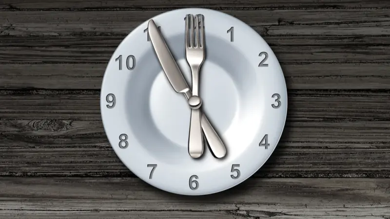 Intermittent fasting and calorie restriction promoting healthy benefits with a clock icon on a plate with knife and fork Intermittent fasting and calorie restriction promoting healthy benefits with a clock icon on a plate with knife and fork