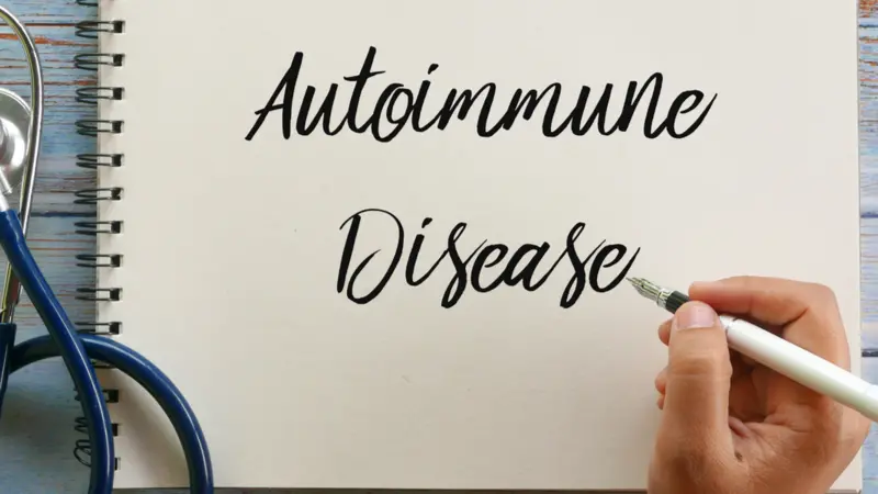 Top view of stethoscope, pen and hand writing ' Autoimmune Disease ' on notebook on wooden background Top view of stethoscope, pen and hand writing ' Autoimmune Disease ' on notebook on wooden background