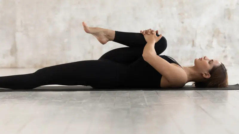 Woman wear black sport clothes lying on floor practising asana 