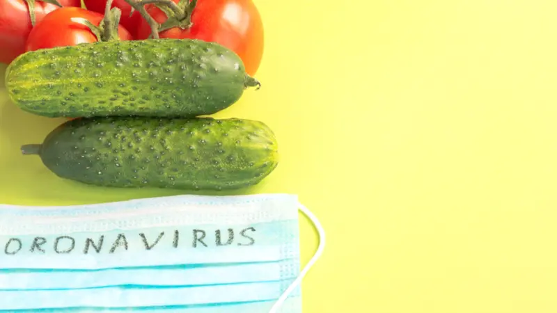 Juicy ripe tomatoes and cucumbers on a green background , next to a protective medical mask with the inscription Coronavirus. 