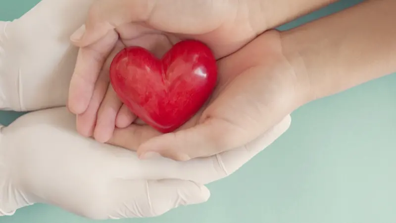 Doctor hands with medical gloves holding child hands and red heart