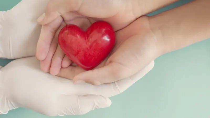 Doctor hands with medical gloves holding child hands and red heart Doctor hands with medical gloves holding child hands and red heart