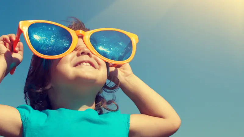 Happy little girl with big sunglasses looking at the sun