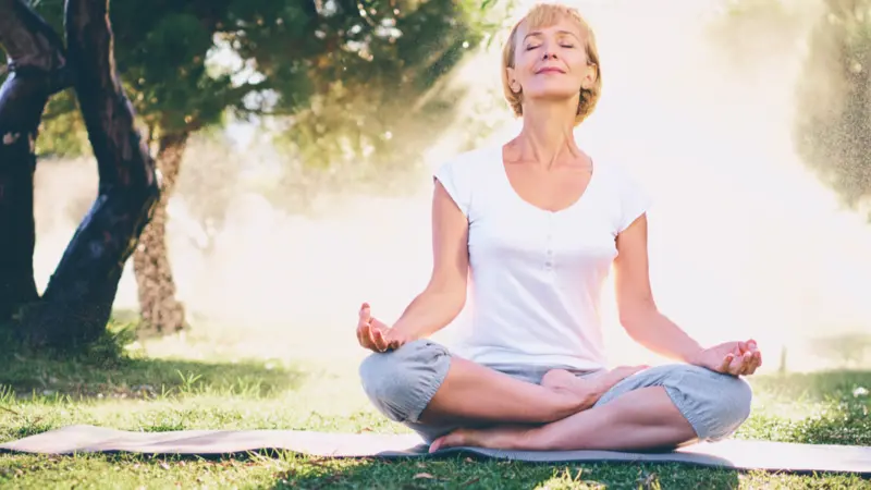 Yoga at park. Senior woman in lotus pose sitting on green grass. 