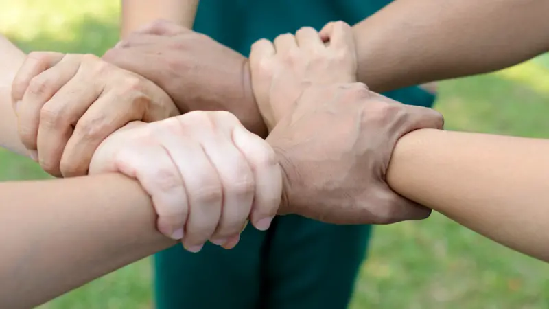 Doctors and nurses in a medical team stacking hands outdoor on the green park background (volunteer)
