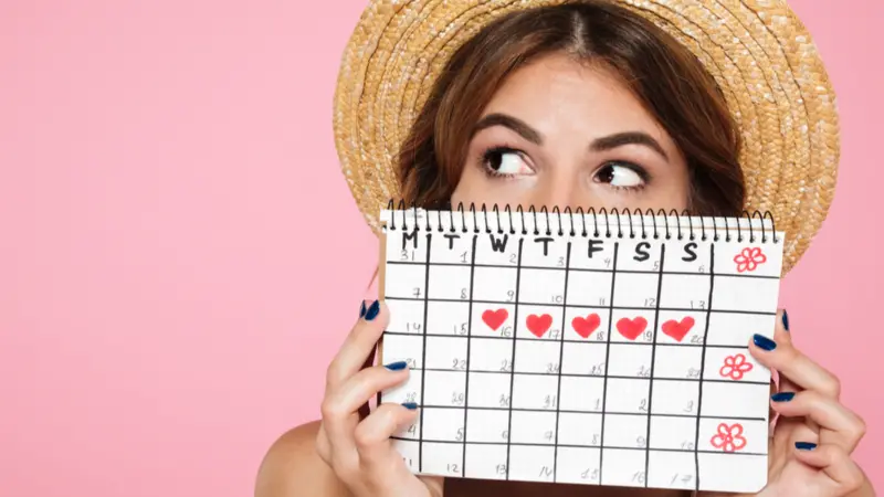 girl in summer hat hiding behind a periods calendar