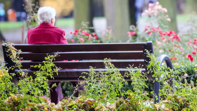 Elderly woman sitting alone on bench in the park