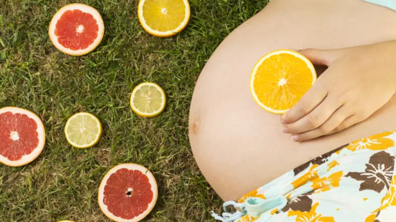 Pregnant woman is laying on grass with fruit