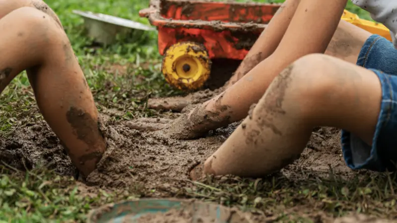 Two boys playing with mud in backyard digging their foot in the dirt.