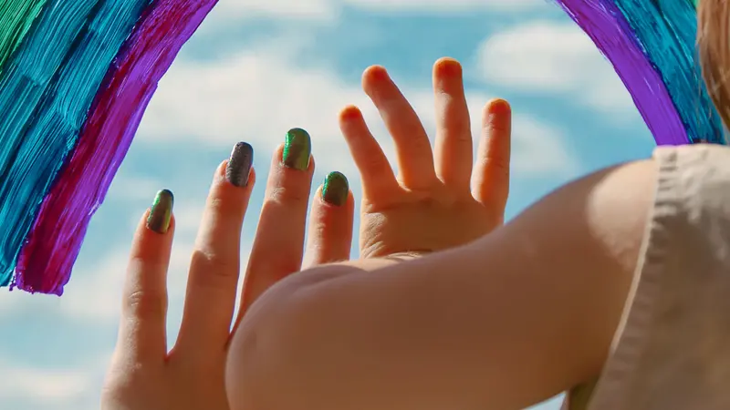 children's hands on the window pane next to a painted colored rainbow