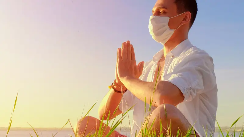 man doing yoga sitting in a lotus pose wearing PPE face mask