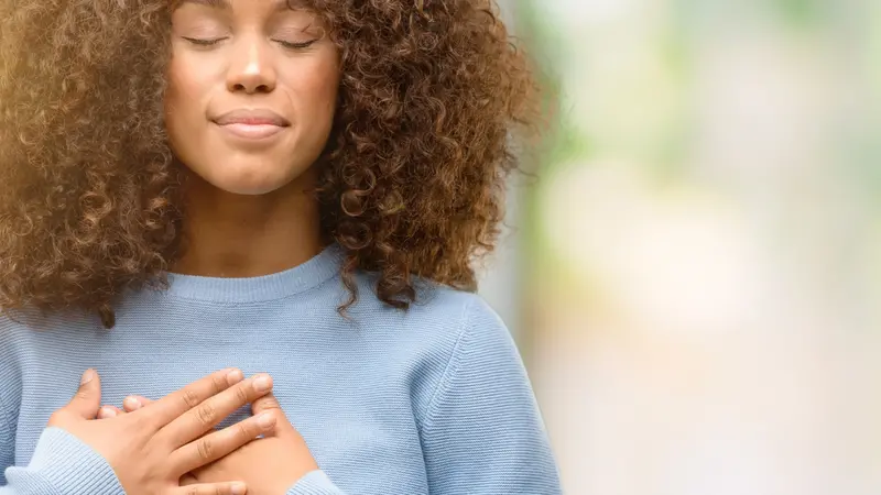 woman wearing a sweater smiling with hands on chest with closed eyes and grateful gesture on face