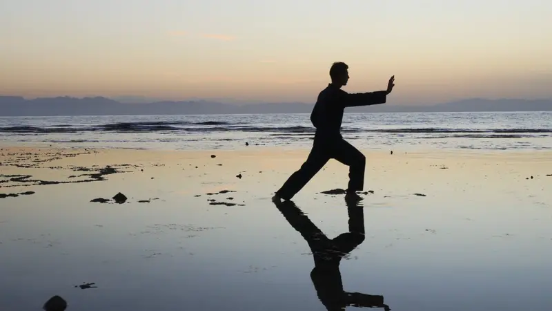 Silhouette of man practicing qigong exercises at sunset by the sea