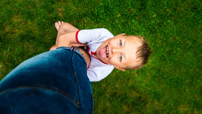 little boy with ADHD hangs on to his fathers leg being playful and full of energy, smiling and happy