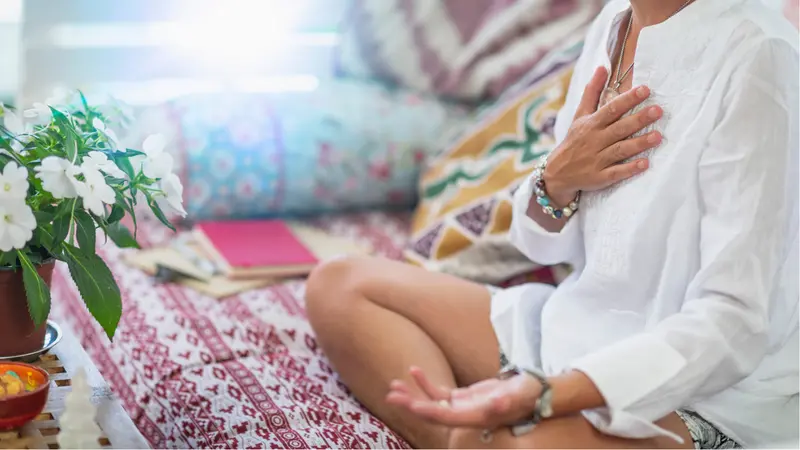 Woman sitting in a lotus position with right hand on heart chakra and left palm open in a receiving gesture