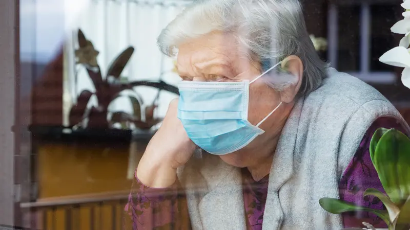 senior woman with surgical mask sitting in window