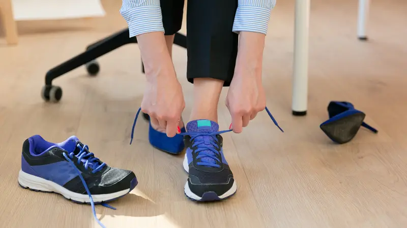 Woman changing high heels, office shoes after working day while sitting on the chair, ready to take a walk or run