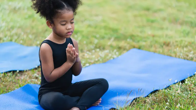 little girl sitting on the roll mat practicing meditate yoga in the park outdoor