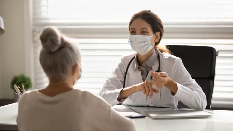 doctor in medical facial mask in consultation with elderly patient during covid-19 pandemic