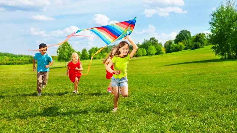 Four little kids running in the park with kite happy and smiling