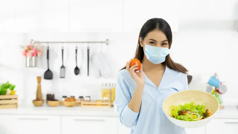 Woman Cooking healthy food in the kitchen and wearing COVID face protection mask 