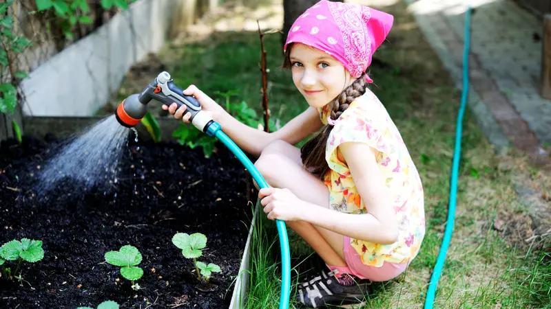 girl, watering the plants, from hose spray in the garden