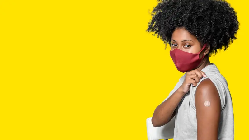 woman wearing protective mask shows the vaccine bandage, isolated on yellow background woman wearing protective mask shows the vaccine bandage, isolated on yellow background