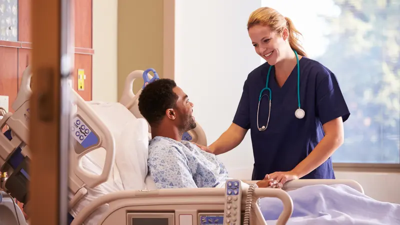 female nurse Talking To Male Patient In Hospital Bed