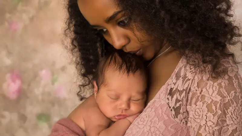 mother in pink lace dress holding her 1 week old little baby