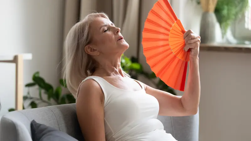 woman using waving fan suffering from hot flash woman using waving fan suffering from hot flash