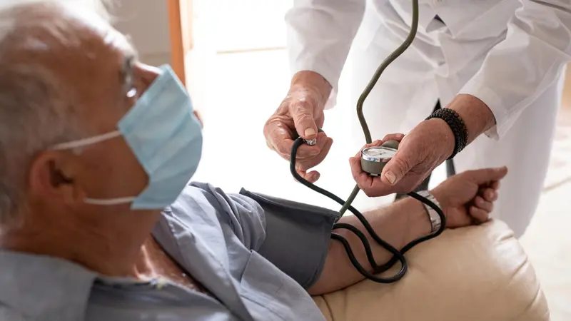 doctor in a white coat takes pressure to an elderly patient with a mask