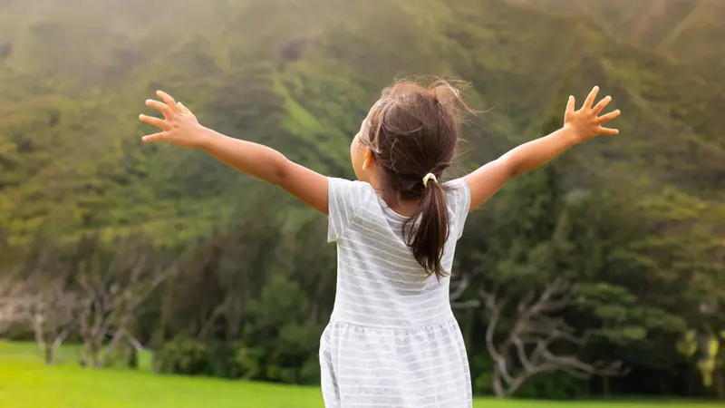 Little girl standing outside, arms raised in gratitude