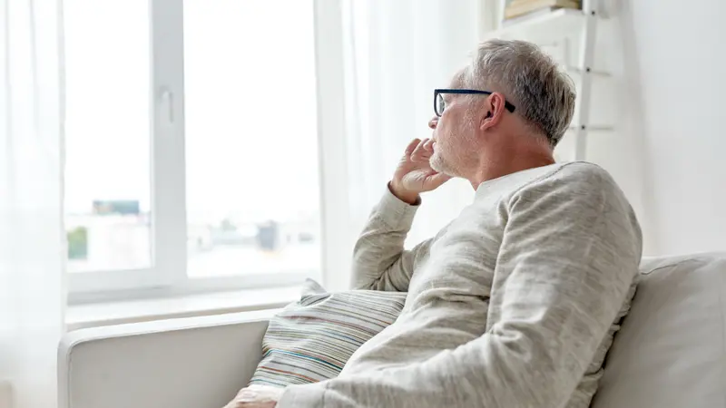 lonely man in glasses thinking and looking through window at home
